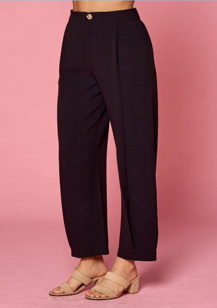 Side view of women's pleated black slacks with side pockets and front pleats with tacked pleat at hem.
