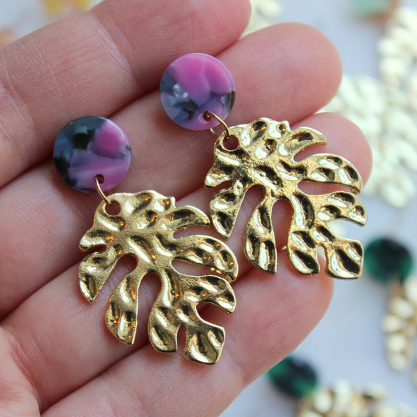 Close up view of gold leaf earrings with hot pink and teal acrylic stud.