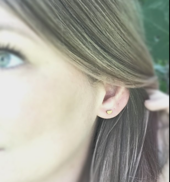 Tiny brass half moon earrings shown on human ear.