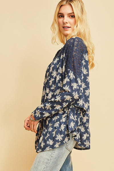 Side view of blue boho top with white floral pattern with ruffled rounded hi-low hem and crochet at shoulder.