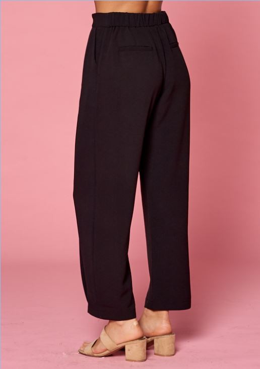 Side back view of women&#39;s pleated black slacks with elastic waist and faux back pockets.