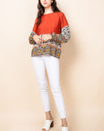 Woman's long sleeved animal and paisley top paired with white pants.