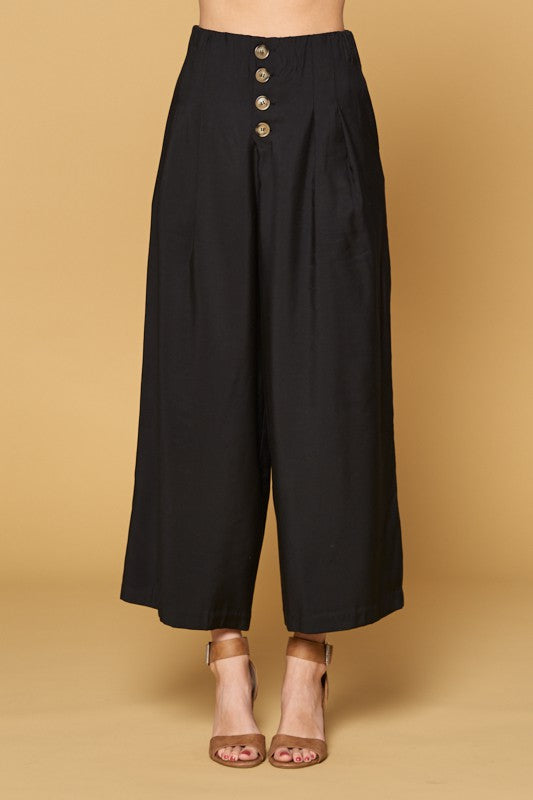 Close up of women&#39;s black button front pants in culotte cut with four button closure and wide legs.