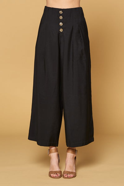Close up of women's black button front pants in culotte cut with four button closure and wide legs.