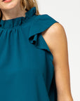 Close up view of ruffle sleeve and ruffle neck blouse in teal.