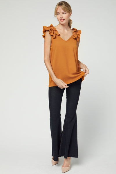 Full view of camel colored sleeveless v-neck top with ruffle at straps with good length for coverage paired with black pants and heels.