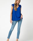 Full view of royal blue top for fall with v-neck and sleeveless ruffle detail paired with jeans and heels. Longer length for coverage.