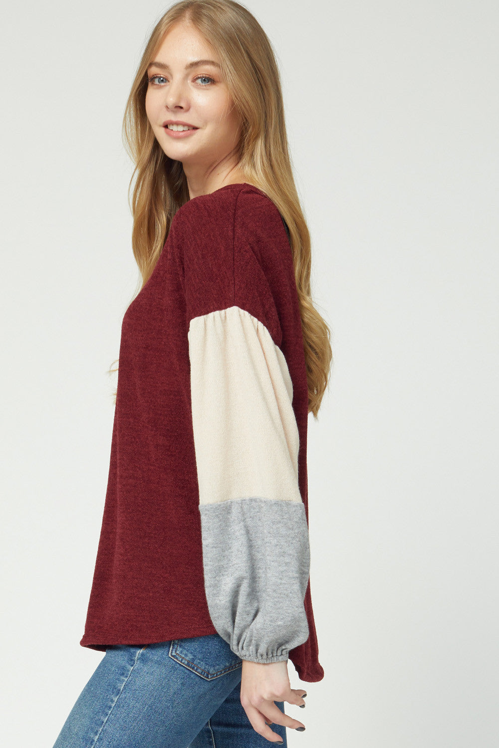 Side view of women's sweater with burgundy bodice and cream and grey color blocked puff sleeves.