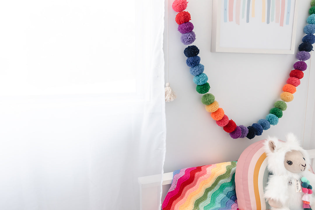 Little girl&#39;s room with rainbow pom pom garland hanging on wall.