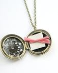 Image of open vintage brass filigree locket with note tied with ribbon inside.