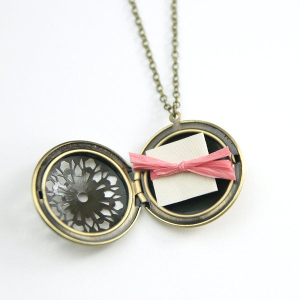 Image of open vintage brass filigree locket with note tied with ribbon inside.