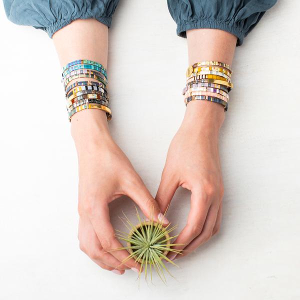 Two wrists wearing large stacks of miyuki bracelets in various colors.