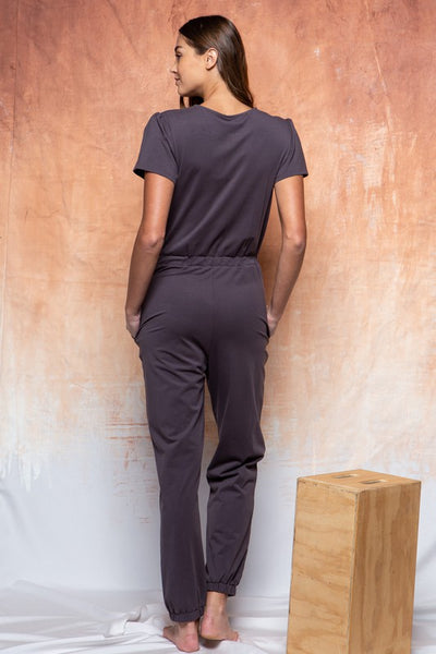 Back view of dark grey knit jumpsuit with elastic waist and pant cuffs with short sleeves and pockets.