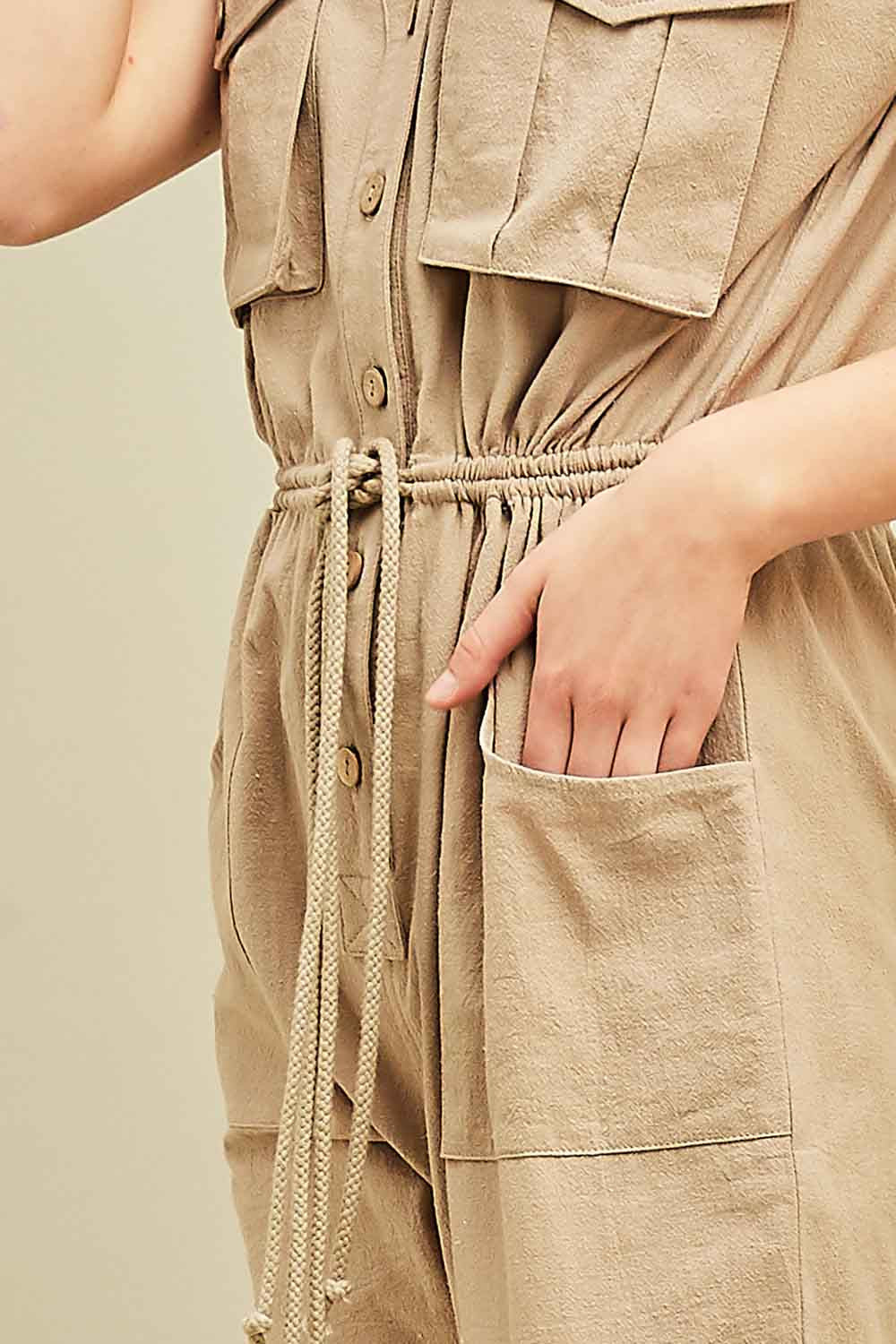 Up close view of women&#39;s cargo jumpsuit in khaki with square pockets at sides and breasts with button front and drawstring waist.