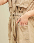 Up close view of women's cargo jumpsuit in khaki with square pockets at sides and breasts with button front and drawstring waist.