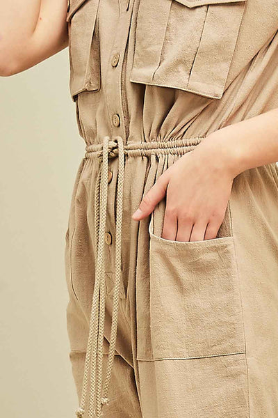 Up close view of women's cargo jumpsuit in khaki with square pockets at sides and breasts with button front and drawstring waist.