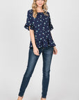 Full view of navy floral peplum top with short ruffle sleeves paired with jeans and heels.