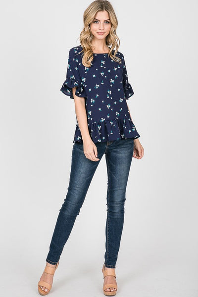 Full view of navy floral peplum top with short ruffle sleeves paired with jeans and heels.