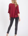 Full back view of burgundy top with ruffled 3/4 sleeve with good back coverage and length paired with black jeans and heels.