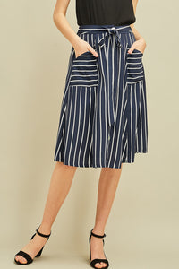 Navy women's midi skirt with vertical white stripes, pockets, elastic waist with tie detail, and buttons up the front.