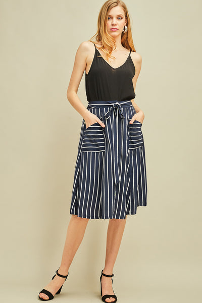 Full view of model wearing women's midi length button up skirt with pockets in navy and white stripe paired with black top and shoes.