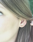 Tiny brass half moon earrings shown on human ear.