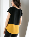 Back view of short sleeve black top with gold contrast hem. Rounded hem with good length for bum coverage.