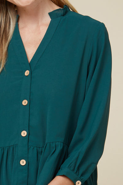 Close up of teal tiered tunic with tan buttons, v-neck, and ruffle detail around collar.