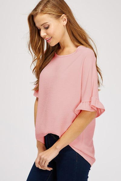 Side view of wide neck, mauve dolman sleeve top with ruffle with front tuck into jeans.