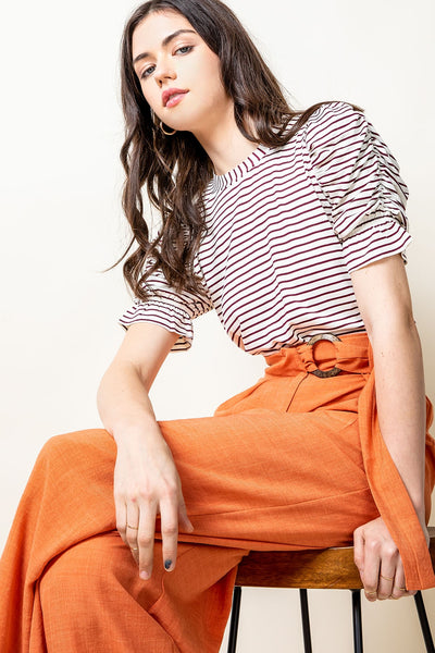 Woman sitting in colorful slacks wearing striped top with short ruched sleeves.