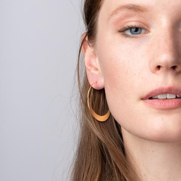 Lightweight hoop earrings worn by model in gold.
