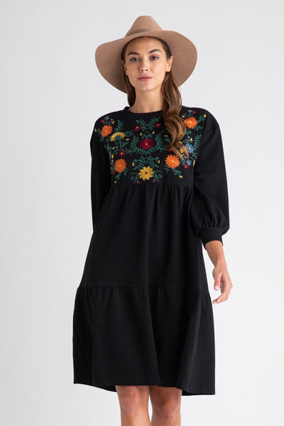 Women's bohemian style dresses with embroidery. Black with floral detail on chest and midi length. Model paired dress with camel colored hat.
