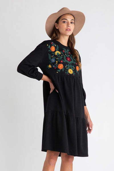 Side view of Women's bohemian style dresses with embroidery. Black with floral detail on chest and midi length tiered skirt.