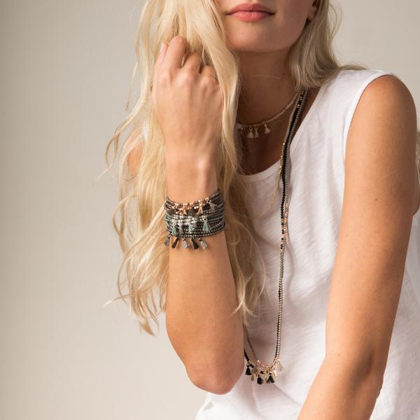 Delicate boho jewelry worn by model. Multiple metallic tassel wraps stacked as bracelets and necklaces.